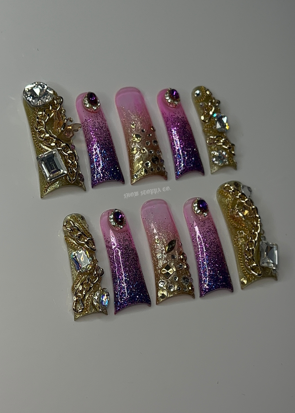 Set of decorative false nails with gold and purple designs on a light gray background
